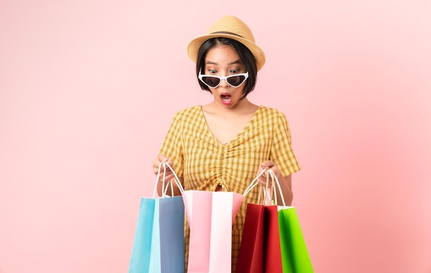 Jeune femme asiatique souriante tenant des sacs à provisions multicolores et regardant sur fond blanc