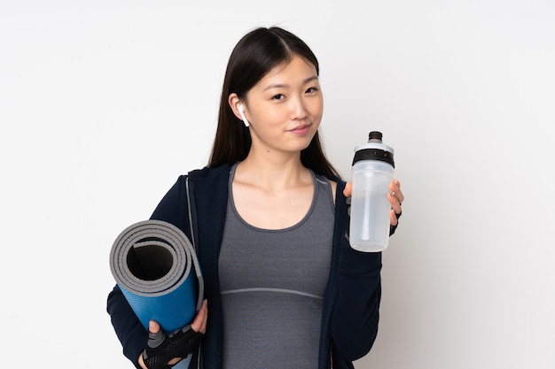 Jeune femme asiatique sport sur mur blanc avec bouteille d'eau de sport et avec un tapis