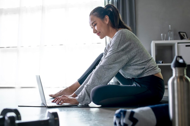 Jeune femme asiatique sportive faisant de l'exercice à la maison en regardant une vidéo de fitness sur Internet ou en suivant un cours de fitness en ligne à l'aide de l'espace de copie intérieur du salon pour ordinateur portable