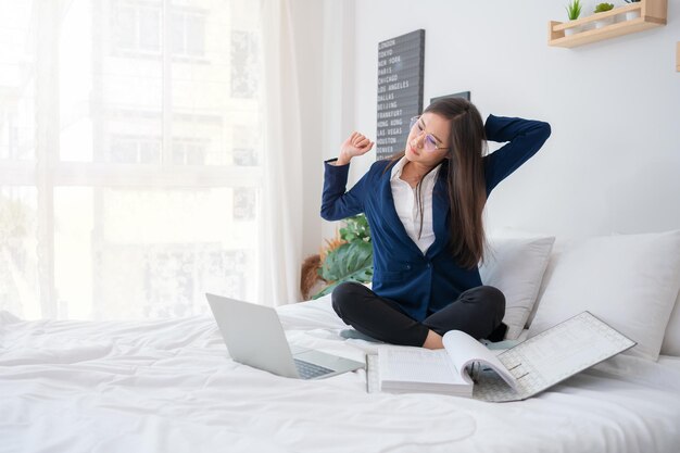 Une jeune femme asiatique surchargée de travail et stressée travaillant sur un ordinateur portable et des documents