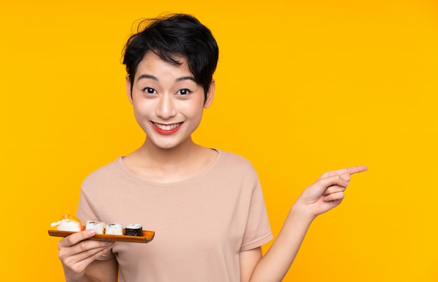 Jeune femme asiatique avec des sushis surpris et pointant le doigt sur le côté