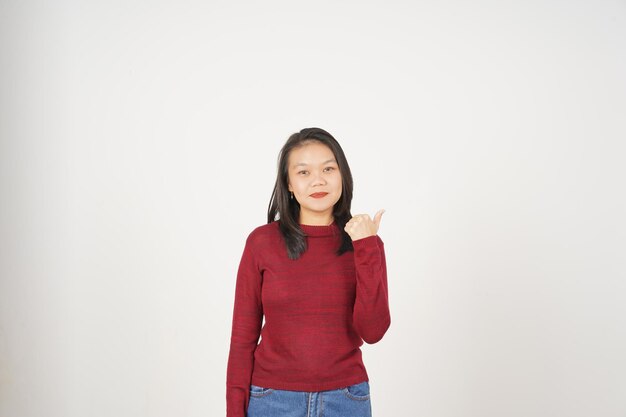 Jeune femme asiatique en t-shirt rouge pointant vers l'espace de copie avec le pouce isolé sur un fond blanc