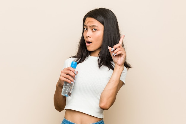 Jeune femme asiatique tenant une bouteille d'eau ayant une excellente idée, concept de créativité.