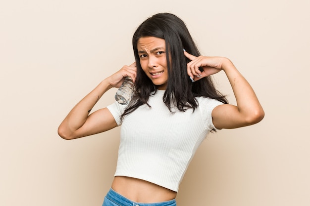 Jeune femme asiatique tenant une bouteille d'eau couvrant les oreilles avec les mains.