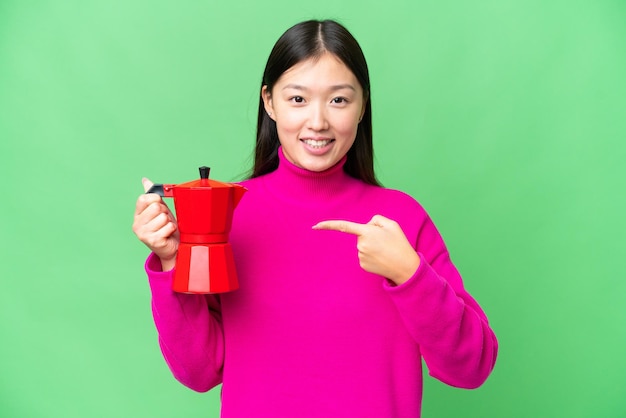 Jeune femme asiatique tenant une cafetière sur fond isolé chroma key et le pointant