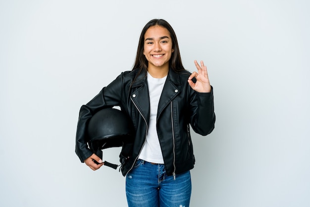 Jeune femme asiatique tenant un casque de moto sur un mur isolé joyeux et confiant montrant le geste ok.