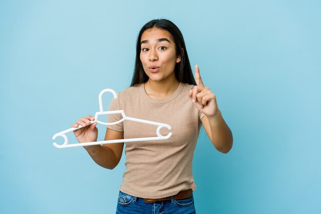 Jeune femme asiatique tenant un cintre isolé sur un mur bleu ayant une idée, un concept d'inspiration