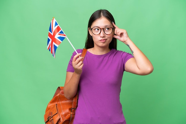 Jeune femme asiatique tenant un drapeau du Royaume-Uni sur fond isolé ayant des doutes et pensant