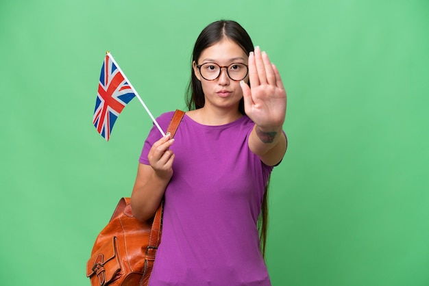 Jeune femme asiatique tenant un drapeau du Royaume-Uni sur fond isolé faisant un geste d'arrêt