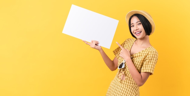 Jeune femme asiatique tenant du papier blanc avec un visage souriant et à la recherche sur le fond jaune