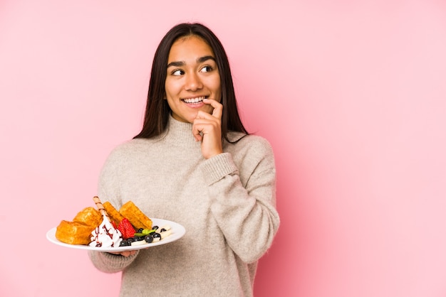 Jeune femme asiatique tenant une gaufre isolée pensée détendue sur quelque chose en regardant un espace de copie