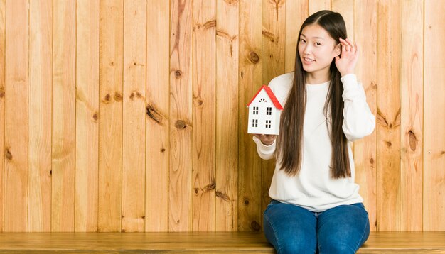 Jeune femme asiatique tenant une icône de la maison essayant d'écouter un potin.