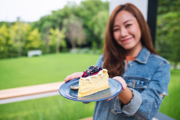 Une jeune femme asiatique tenant et montrant une assiette de gâteau au fromage aux bleuets