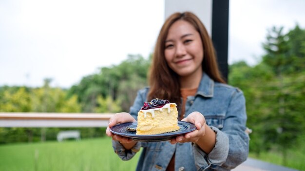 Une jeune femme asiatique tenant et montrant une assiette de gâteau au fromage aux bleuets