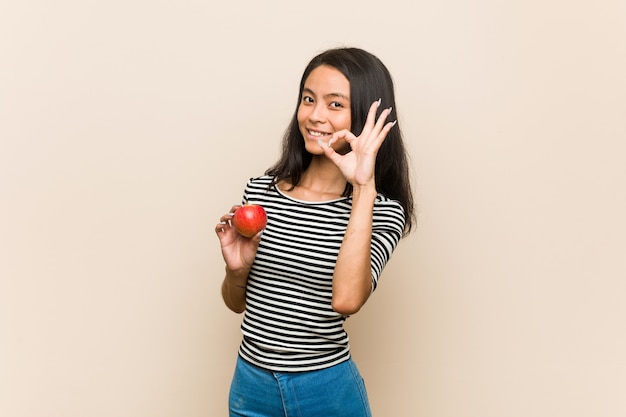 Jeune femme asiatique tenant une pomme gaie et confiante montrant le geste ok.