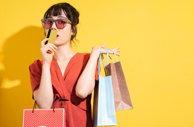 Jeune femme asiatique tenant des sacs à provisions posant sur jaune