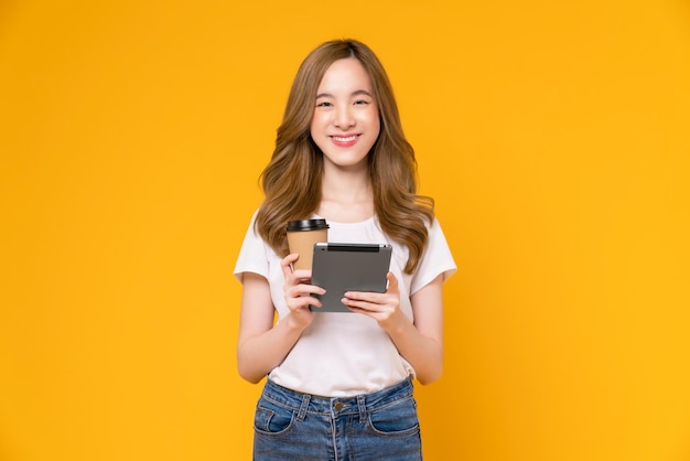 Photo jeune femme asiatique tenant une tablette numérique et une tasse de café avec écran tactile sur fond jaune clair