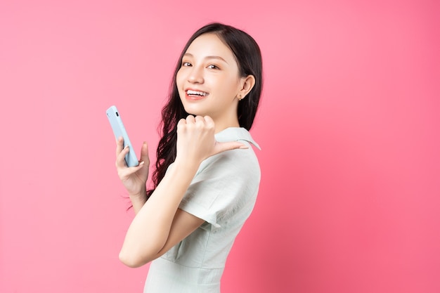 Jeune femme asiatique tenant le téléphone à la main et pointant vers l'arrière sur rose