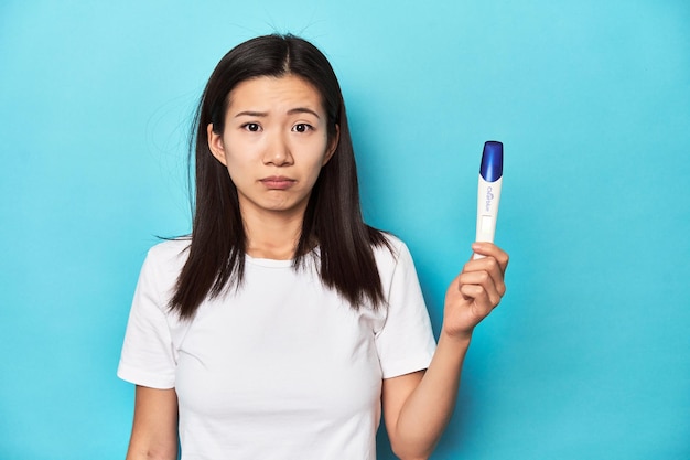 Une jeune femme asiatique tenant un test de grossesse filmé en studio