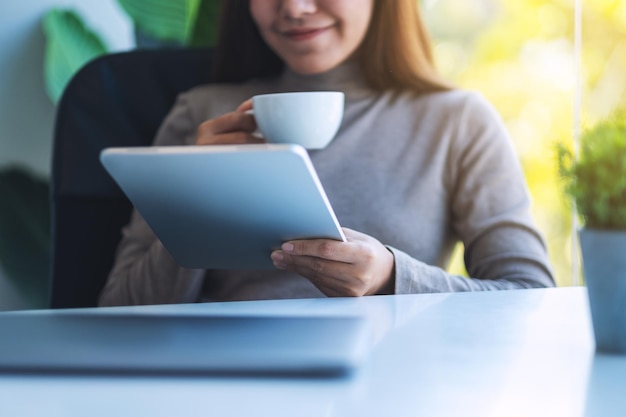 Une jeune femme asiatique tenant et utilisant un Tablet PC avec un ordinateur portable sur la table au bureau