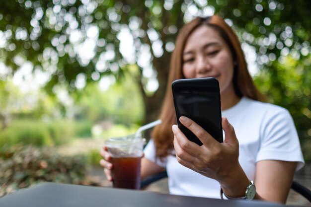 Une jeune femme asiatique tenant et utilisant un téléphone intelligent tout en buvant du café à l'extérieur