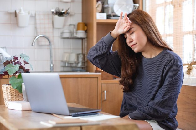 Une jeune femme asiatique tombe malade et stressée en travaillant ou en étudiant en ligne sur un ordinateur portable à la maison