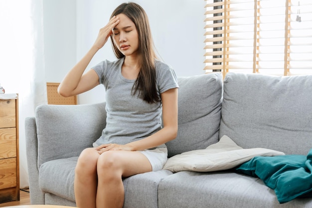 Jeune femme asiatique touchant le front ayant des maux de tête migraine et bouleversée par le problème se sentir stressée assise sur un canapé dans le salon à la maison personnes dépression douloureuse concept médical et de soins de santé