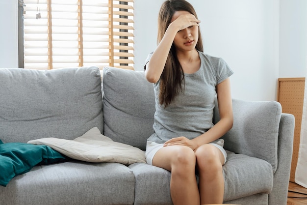 Jeune femme asiatique touchant le front ayant des maux de tête migraine et bouleversée par le problème se sentir stressée assise sur un canapé dans le salon à la maison personnes dépression douloureuse concept de soins médicaux et de santé