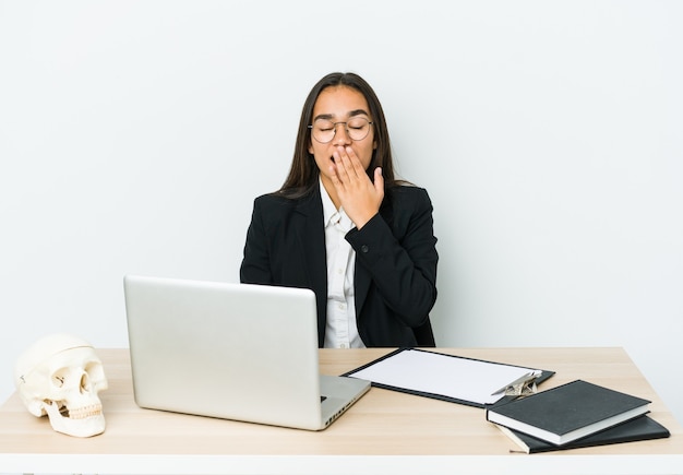 Jeune femme asiatique traumatologue isolée sur un mur blanc bâillant montrant un geste fatigué couvrant la bouche avec la main.