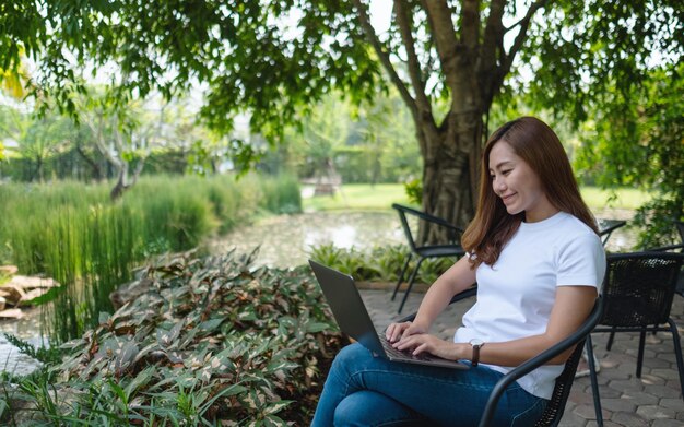 Une jeune femme asiatique travaillant et tapant sur un clavier d'ordinateur portable assis dans le parc