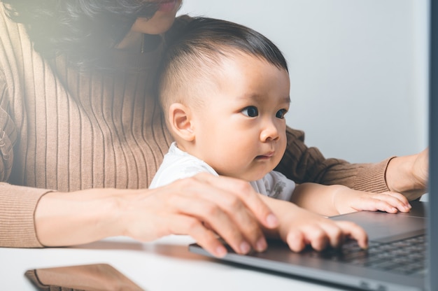 Jeune femme asiatique travaille à domicile tout en gardant un ordinateur portable de jeu dans le concept de famille.Mère enseignant à son fils pour l'utilisation d'Internet.