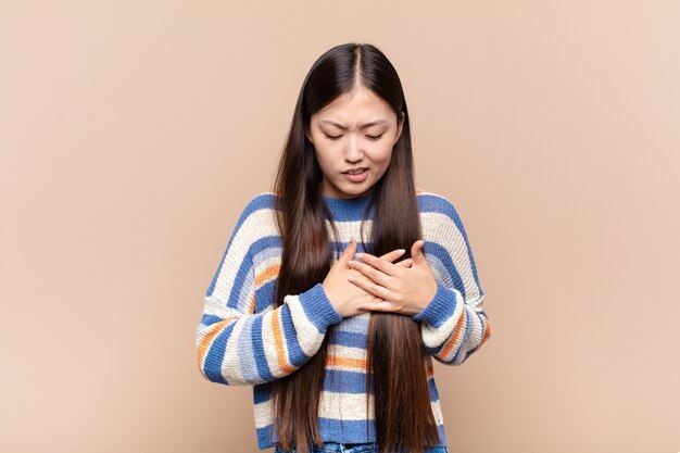 Jeune femme asiatique à la triste, blessée et le cœur brisé, tenant les deux mains près du cœur, pleurer et se sentir déprimé