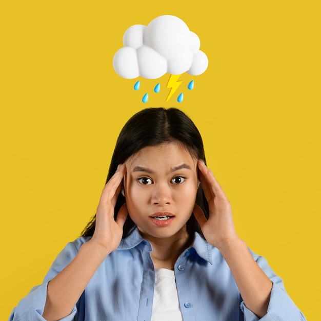 Une jeune femme asiatique triste et choquée tient la tête avec les mains avec un nuage abstrait d'éclairs et de signe de pluie