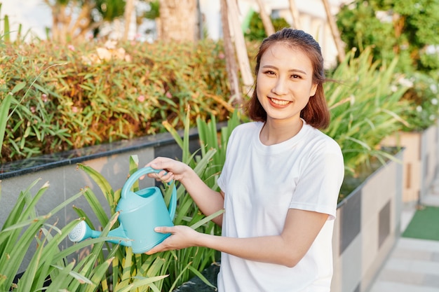 Jeune femme asiatique en tshirt blanc arrosant des plantes dans son jardin.