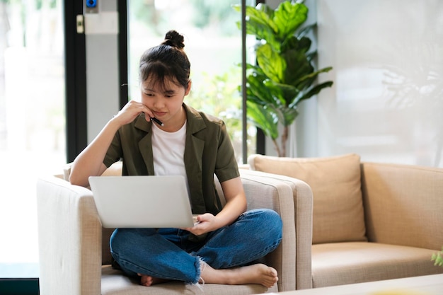 Jeune femme asiatique utilisant un ordinateur portable tout en se penchant en arrière sur un canapé à homexA