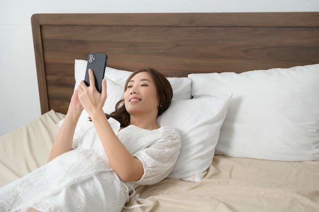 Jeune femme asiatique utilisant un smartphone avant le concept de mode de vie heureux au coucherx9