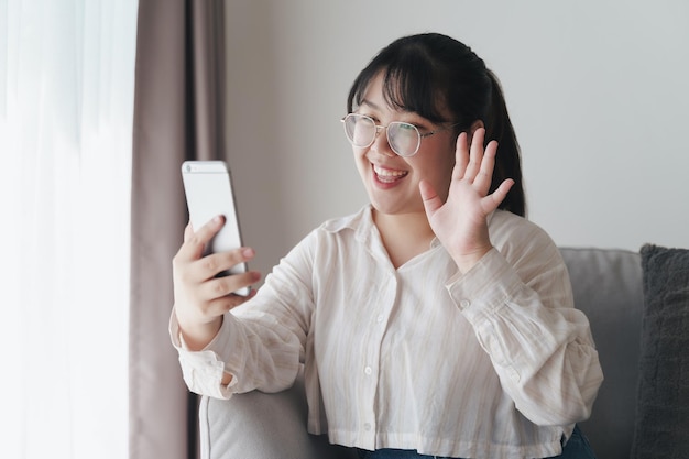 Jeune femme asiatique utilisant un smartphone pour une visioconférence en ligne en agitant la main faisant un geste de bonjour