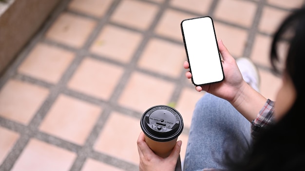 Jeune femme asiatique utilisant son smartphone et sirotant un café tout en se relaxant au café