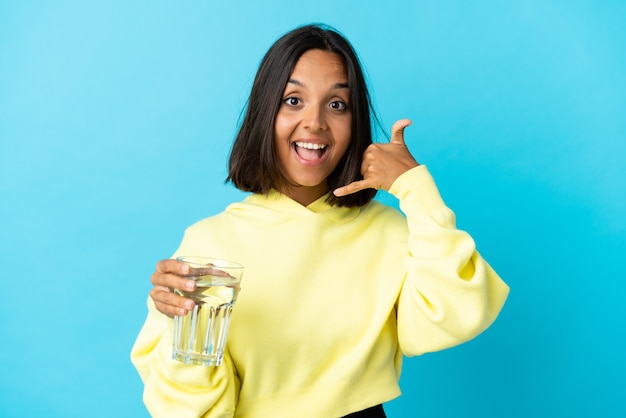 Jeune femme asiatique avec un verre d'eau isolé sur bleu faisant le geste du téléphone. Rappelez-moi signe