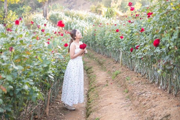 Jeune femme asiatique vêtue d'une robe blanche pose avec une rose dans la roseraie