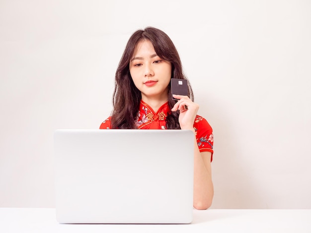 Jeune femme asiatique vêtue d'une robe traditionnelle cheongsam qipao à l'aide d'un ordinateur portable et d'un concept de commerce électronique en ligne par carte de crédit isolé sur fond blanc