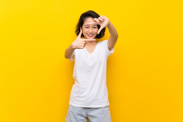 Jeune femme asiatique sur le visage isolé de mur jaune. Symbole d&#39;encadrement