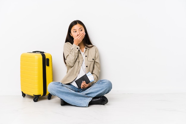 Jeune femme asiatique voyageur assis tenant une carte d'embarquement réfléchie et couvrant la bouche avec la main