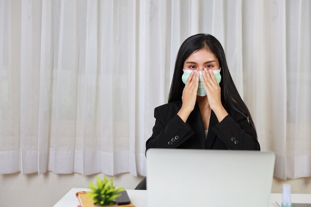 Jeune femme asiatique waring protéger le masque assis au bureau et travaillant sur ordinateur portable et smartphone.