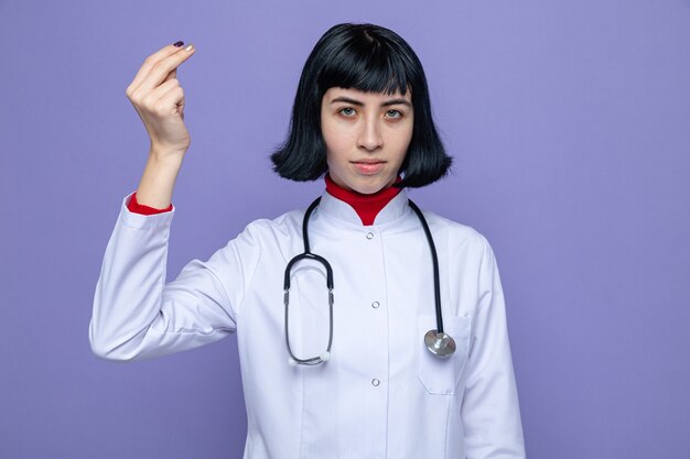 Jeune femme assez caucasienne confiante en uniforme de médecin avec stéthoscope faisant semblant de tenir quelque chose