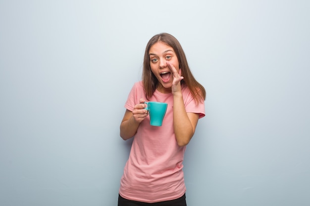 Jeune femme assez caucasienne criant quelque chose de joyeux à l'avant. Elle tient une tasse.