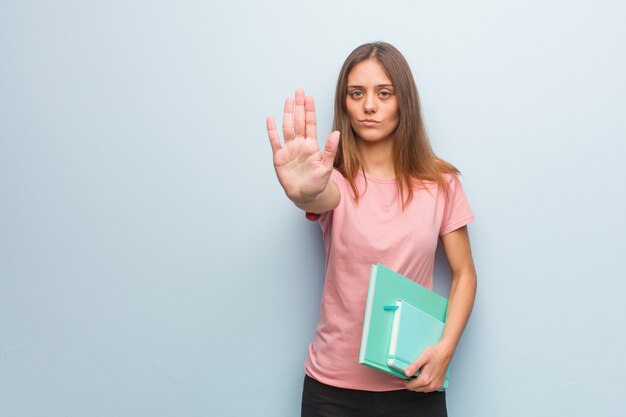 Jeune femme assez caucasienne mettant la main devant. Elle tient des livres.