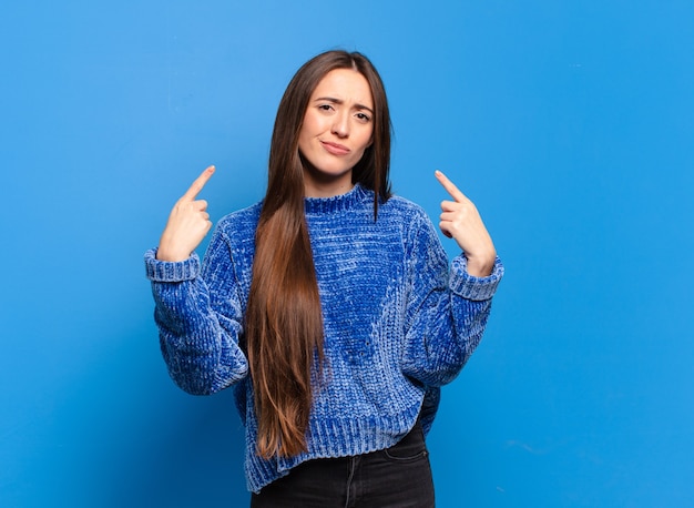 Jeune femme assez décontractée avec une mauvaise attitude, fière et agressive, pointant vers le haut ou faisant un signe amusant avec les mains