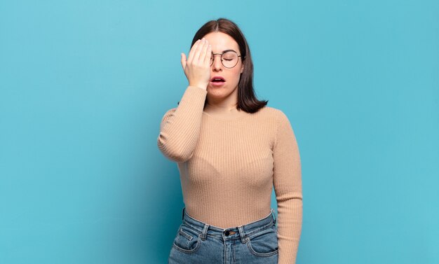 Jeune femme assez décontractée qui a l'air endormie, ennuyée et bâillante, avec un mal de tête et une main couvrant la moitié du visage
