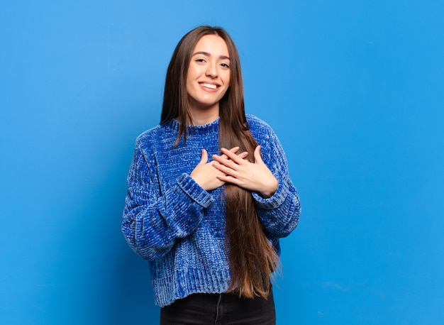 Jeune femme assez décontractée se sentir romantique, heureuse et amoureuse, souriant joyeusement et se tenant la main près du cœur